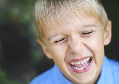 little boy in blue laughs and shows his missing tooth