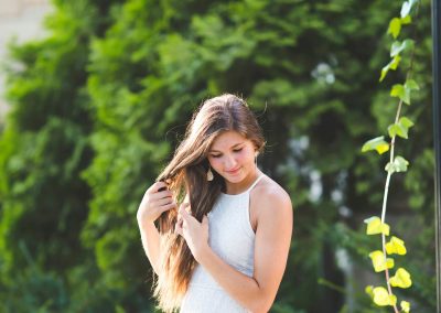 senior girl in white dress plays with hair