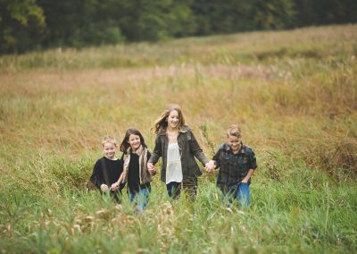 kids run through a hay field holding hands